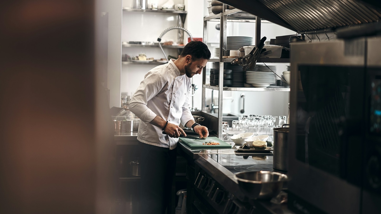 A chef in whites working a station in a professional restaurant kitchen, the back of house a kitchen manager runs